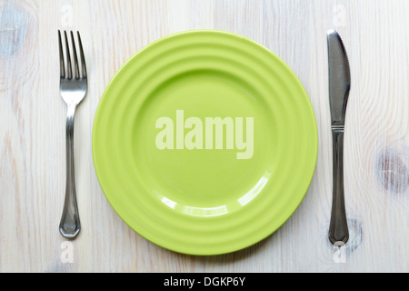 green empty dish-plate on the vintage wooden table with fork and knife