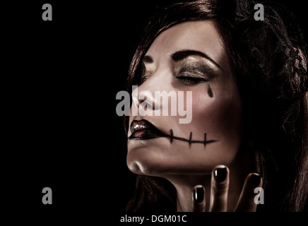 Evil witch on black background, closeup portrait of young beautiful girl with terrifying makeup, closed eyes, Halloween party Stock Photo