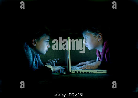 Children at the computer, lying on the sofa in the dark Stock Photo