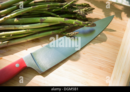 On the farm. A chopping board and sharp kitchen knife. A bunch of freshly picked organic asparagus. Stock Photo