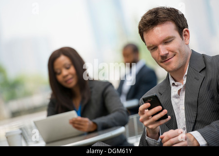 Summer. Three people sitting outside working. Using a digital tablet and smart phones. Stock Photo