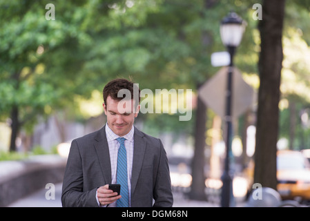 Summer. A young man in a grey suit and blue tie. Using a smart phone. Stock Photo