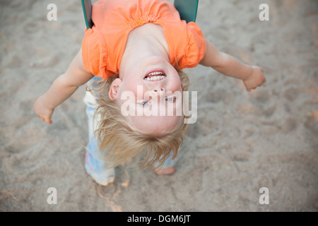 A child playing outdoors. A girl hanging upside down on a swing. Stock Photo