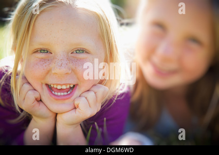 Two young girls, with blue eyes and blonde hair. Lying on the grass. Close up.