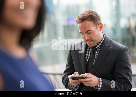 A man in a suit checking his phone. A woman in the foreground. Stock Photo