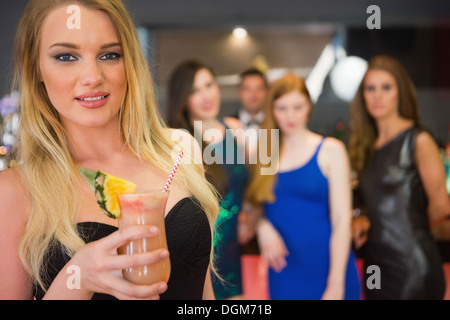Blonde woman standing in front of her friends holding cocktail