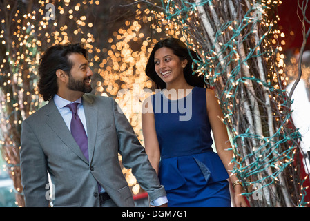 Business people. Two people, a man and woman holding hands and walking under a pergola, lit with fairy lights.