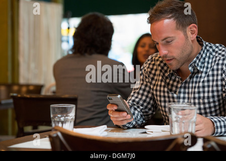 Business people. Two people talking to each other, and a man at a separate table checking his phone. Stock Photo