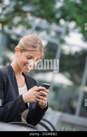 A young blonde businesswoman on a New York city street. Wearing a black jacket. Using a smart phone. Stock Photo