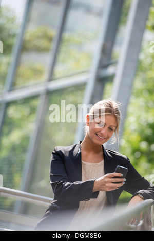 A young blonde businesswoman on a New York city street. Wearing a black jacket. Using a smart phone.
