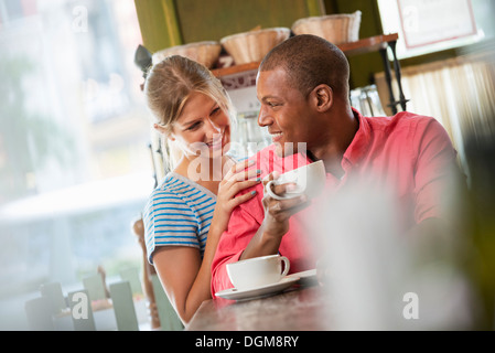Two people, a man and woman seated close together, looking at each other. Having a cup of coffee. Stock Photo
