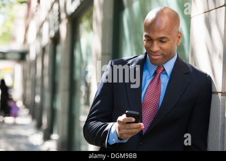 Business people. A businessman in a suit and red tie, checking his phone. Stock Photo
