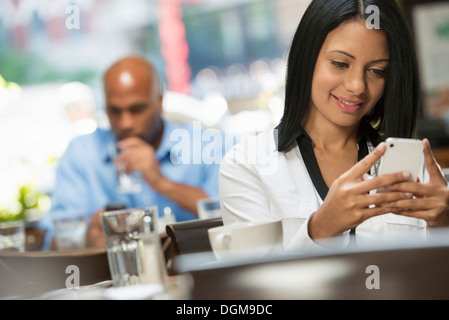 Business people. Two people sitting at coffee shop tables, checking their messages. Stock Photo