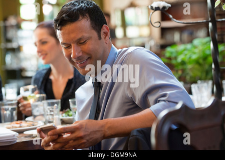 Business people. Three people around a cafe table, one of whom is checking their phone. Stock Photo
