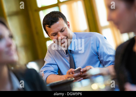 Business people. Three people around a cafe table, one of whom is checking their phone. Stock Photo