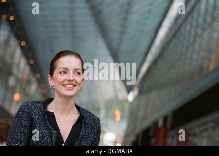 Business people outdoors. A woman in a grey jacket with her hair up, smiling. Stock Photo