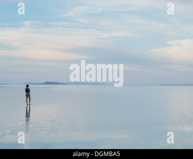 A woman standing on the flooded Bonneville Salt Flats at dusk. Reflections in the shallow water. Stock Photo
