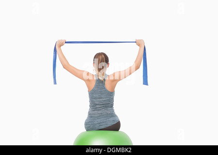 Ponytailed woman training using a resistance band sitting on a fitness ball Stock Photo