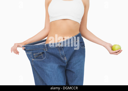 Mid section of slim woman wearing too big jeans holding an apple Stock Photo