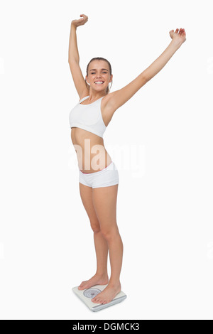 Happy slim woman standing on a scales spreading her arms Stock Photo