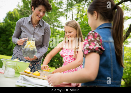 A summer family gathering at a farm. A woman and two children standing outside by a table, laying the table. Making lemonade. Stock Photo