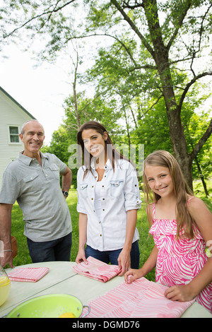 A summer family gathering at a farm. Three people standing by a table, father and daughters. Two girls and a mature man. Stock Photo