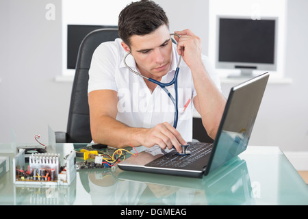 Handsome stern computer engineer examining laptop with stethoscope Stock Photo