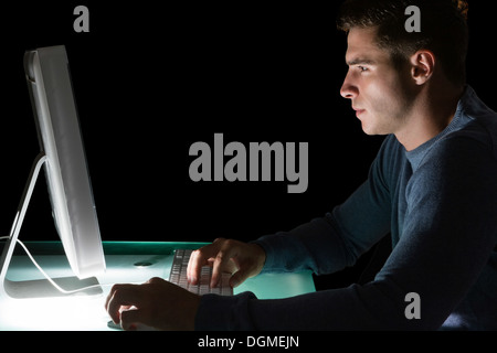 Handsome serious computer engineer looking at computer at night Stock Photo