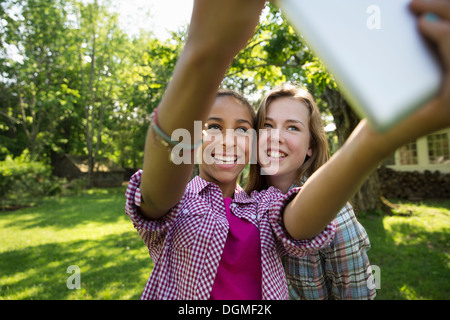 Two girls sitting outdoors on a bench, using a digital tablet. Holding it out at arm's length. Stock Photo