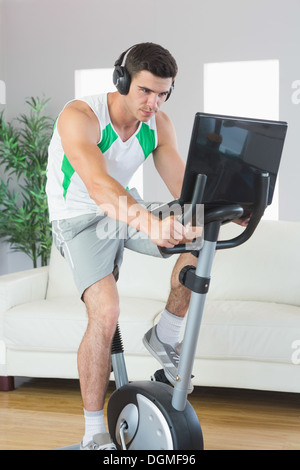 Determined handsome man training on exercise bike using laptop Stock Photo