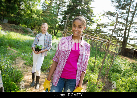 Two girls in a garden, walking up the path, one carrying a plant in a pot. Stock Photo