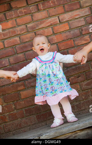 Girl, 1, standing with her hands being held Stock Photo