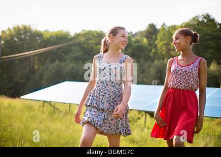 Two young girls on the farm, outdoors. A large solar panel in the field behind them.
