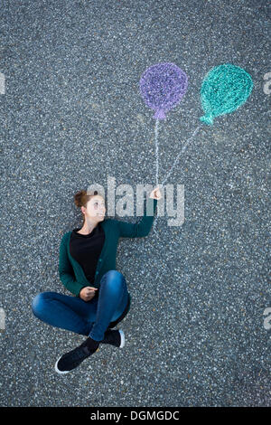 Young woman appearing to be suspended from two painted balloons, taken from above Stock Photo