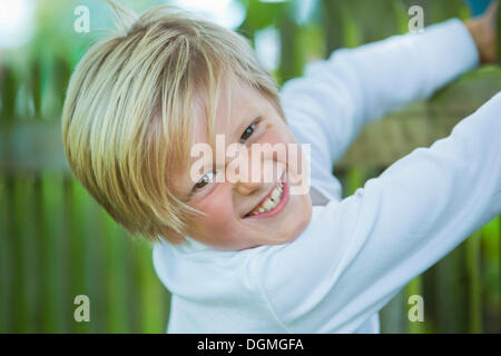 Boy, 7 years old, hanging on to a wooden fence Stock Photo