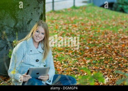 Young woman leaning against a tree in the park with a tablet PC Stock Photo