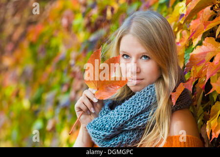 Young woman wearing a thick scarf and holding an autumnal coloured leaf in her hand Stock Photo