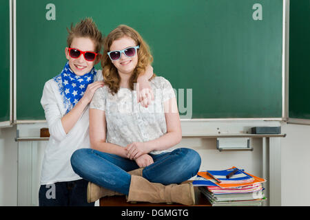 Boy embracing a girl in the classroom, both are wearing sunglasses, Germany Stock Photo