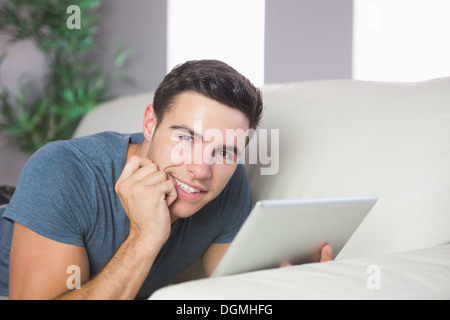 Smiling handsome man lying on couch using tablet Stock Photo