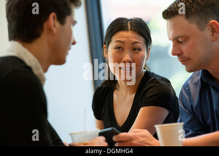 A group of people sitting around a table in a coffee shop. Looking at the screen of a digital tablet. Stock Photo
