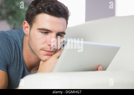 Focused handsome man lying on couch using tablet Stock Photo