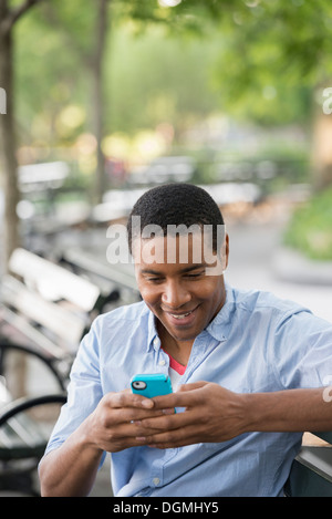 Summer in the city. A man sitting on a bench using a smart phone. Stock Photo