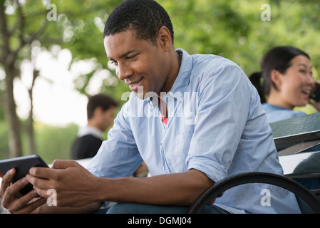 Summer. A man sitting on a bench using a digital tablet. Stock Photo