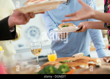 An informal office event. People handing plates of food across a buffet table. Stock Photo