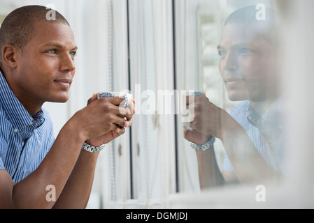Office. A young man leaning on the windowsill holding a cup of tea. Stock Photo