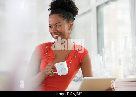 A young woman in a pink shirt using a digital tablet, holding a cup of coffee. Stock Photo