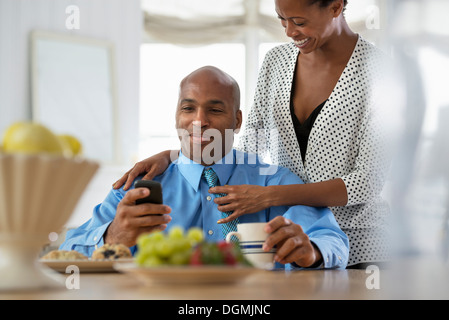 A man in a blue shirt, sitting at a breakfast bar using a smart phone.