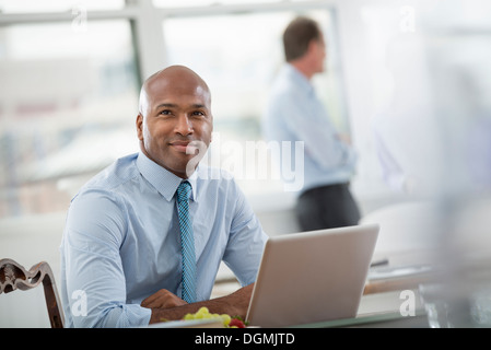 Office life. Businessman in a shirt and tie sitting at a desk, using a laptop computer. Stock Photo