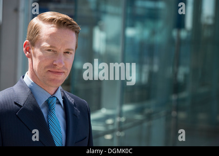 A man in a business suit outside a building with a glass exterior. Stock Photo