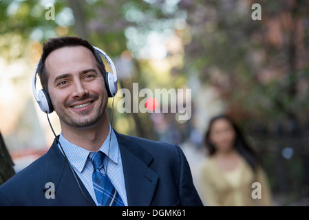 A man in a business suit wearing white headphones, listening to music. Stock Photo